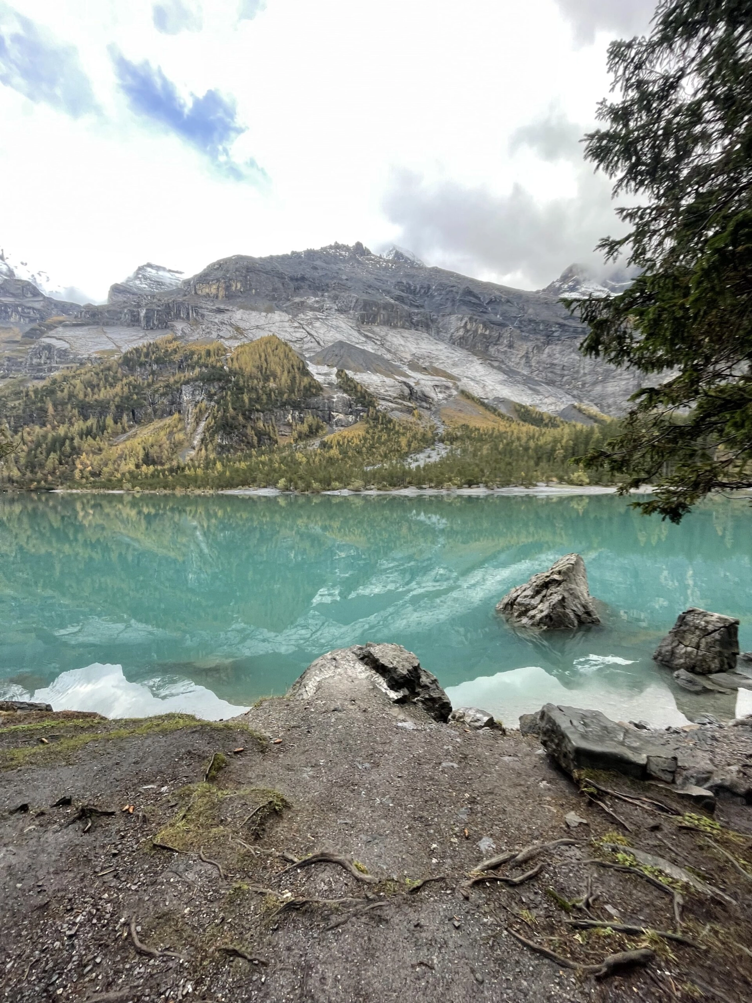 Türkisfarbener Bergsee mit Felsen im Vordergrund und herbstlichen Hängen.