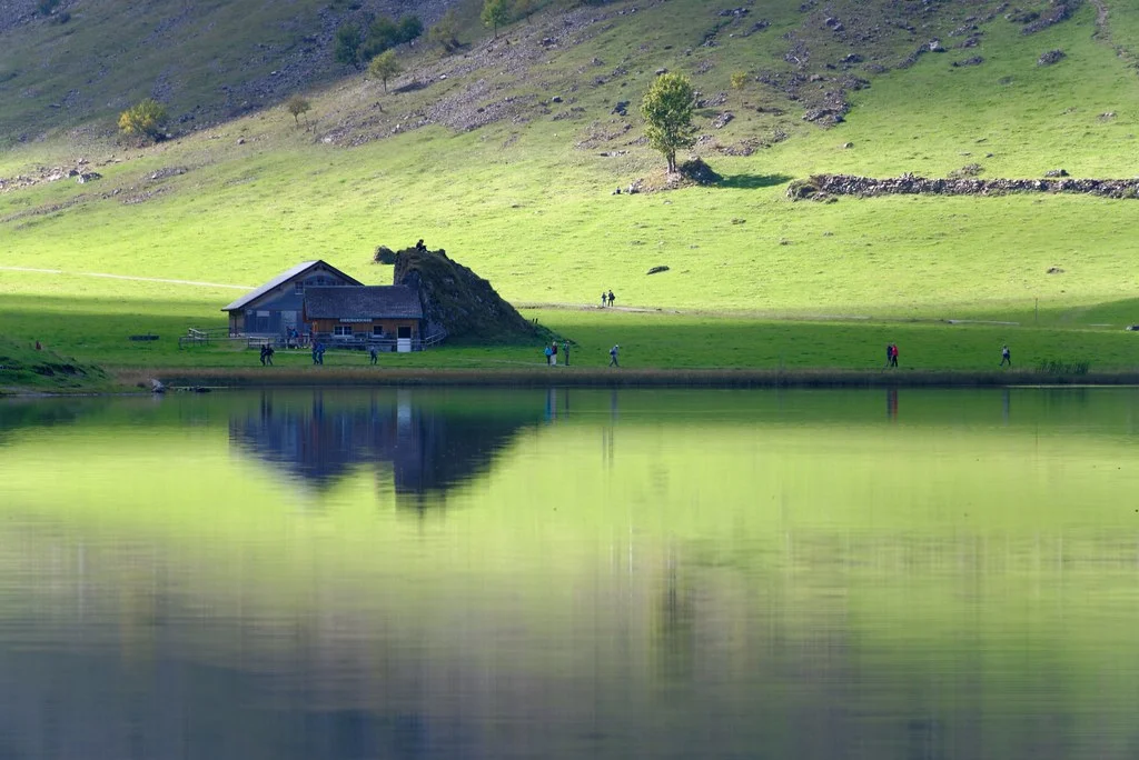 Alpsee mit Berghütte und Spiegelung im ruhigen Wasser.
