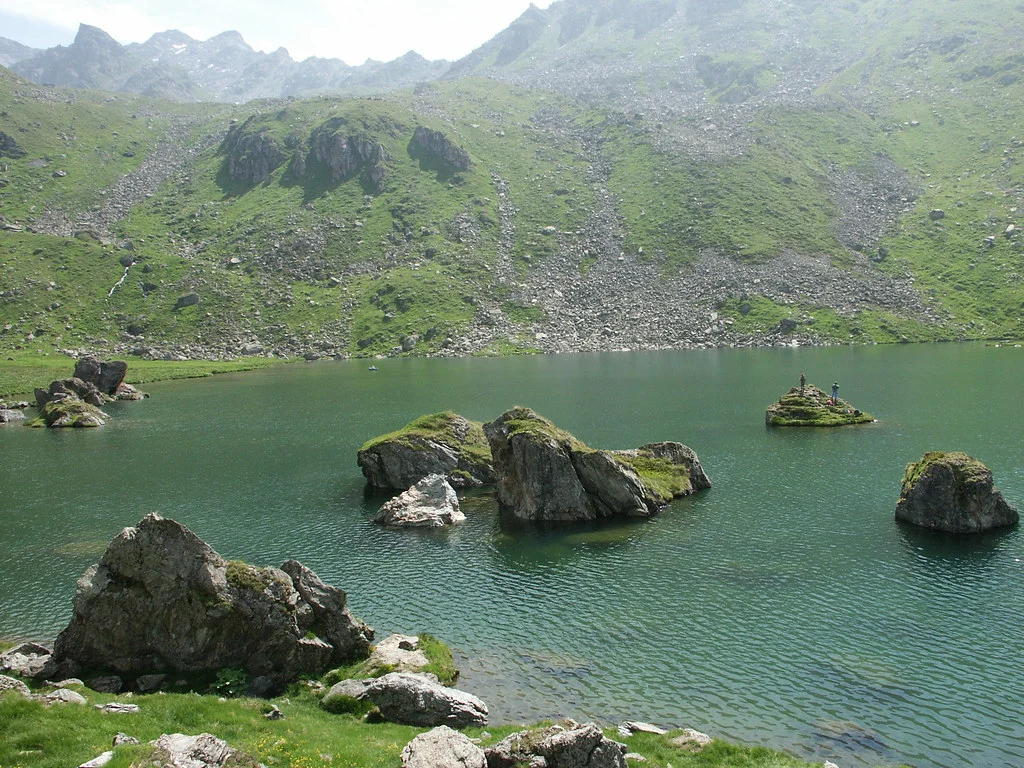 Lac de Louvie: Bergsee mit Felseninseln und grünen Hängen im Hintergrund.