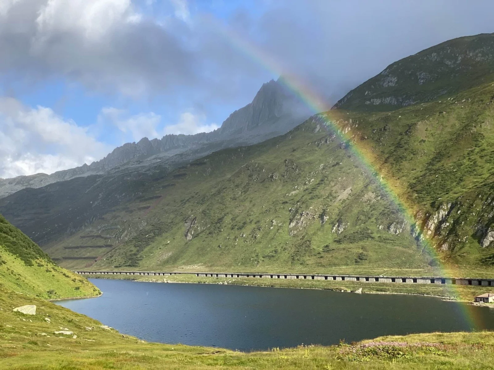 Regenbogen über dem Oberalpsee mit Bergen im Hintergrund