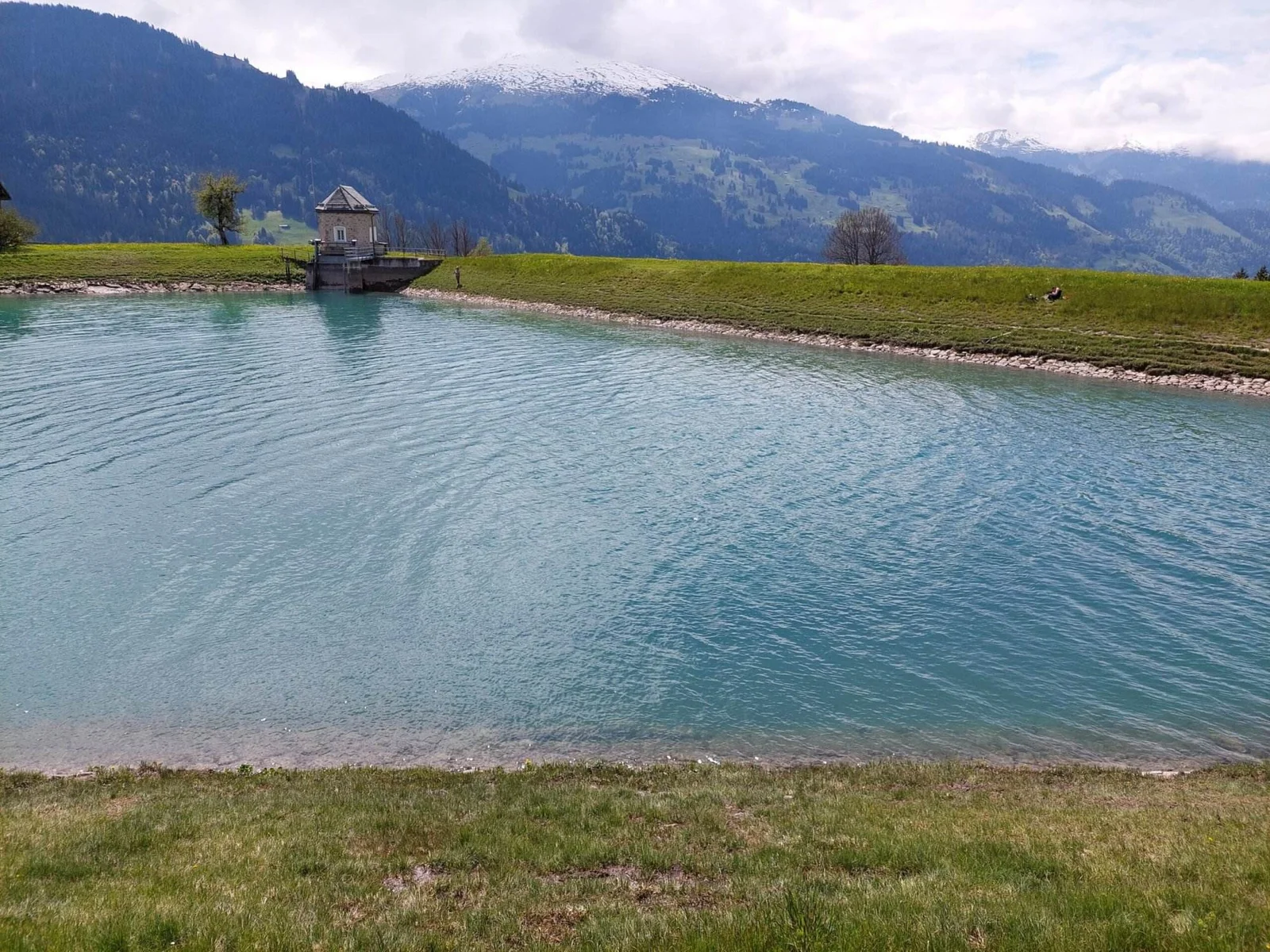 Blauer Plävigginsee mit Staumauer und Bergpanorama im Hintergrund.