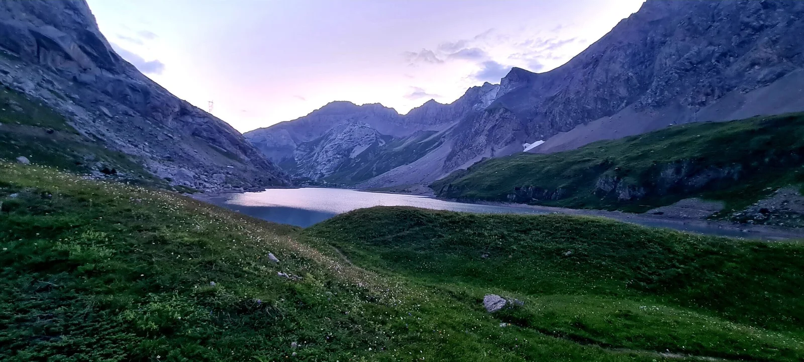 Lac de Sanetsch: Bergsee umgeben von grünen Wiesen und steilen Felswänden in der Abenddämmerung.