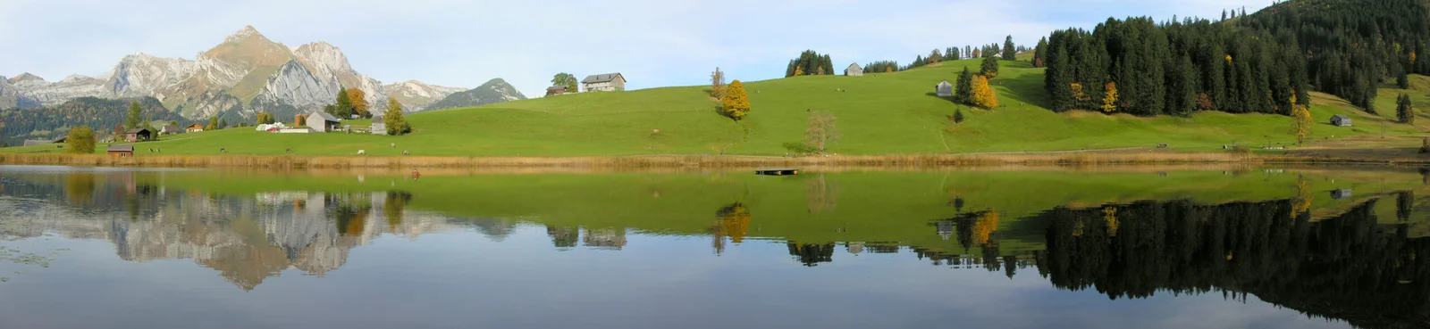 Spiegelung des Schwendisees mit Bergen, Wiesen und Bäumen im Wasser.
