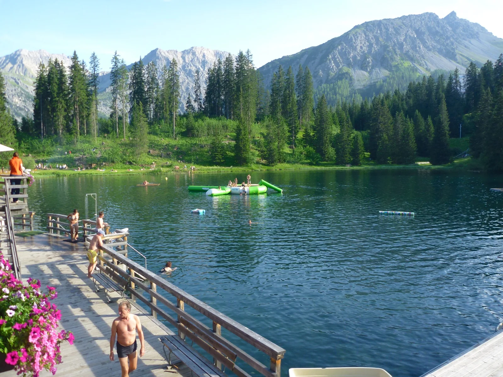 Untersee Arosa: Badegäste genießen den See vor Bergkulisse und Wald.