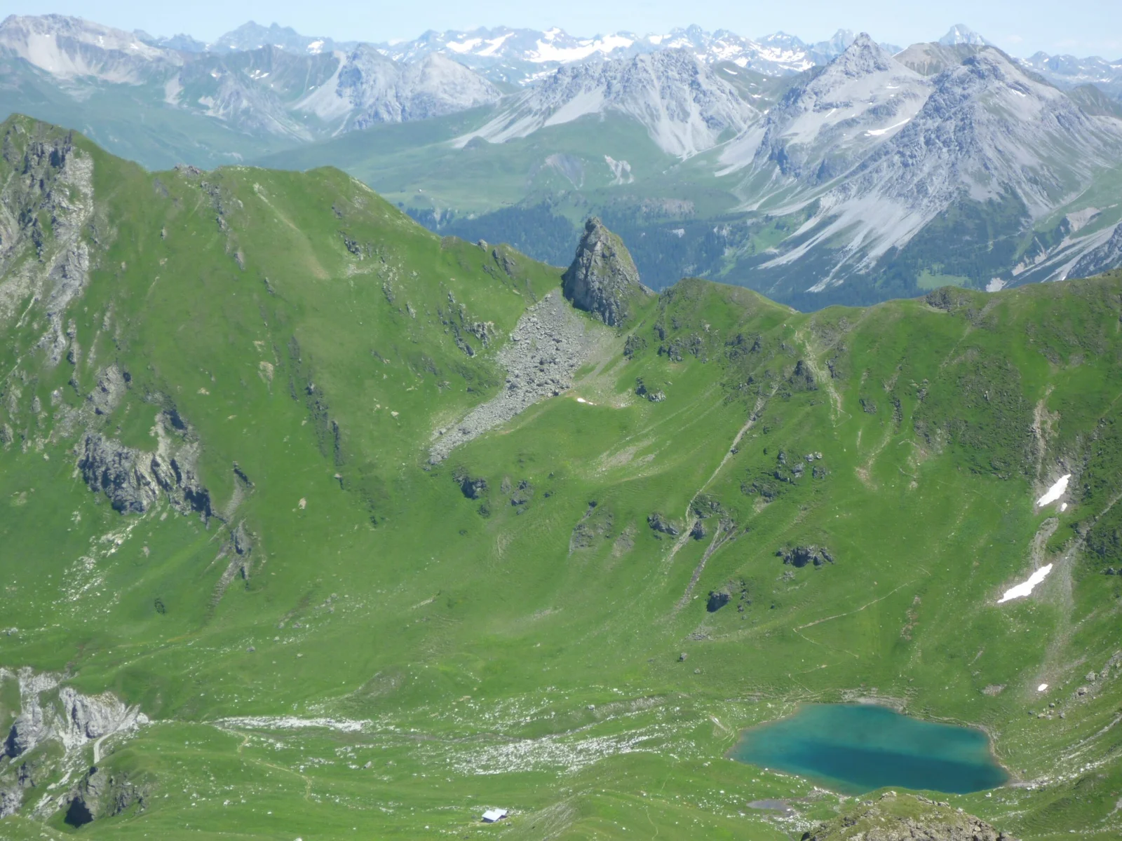 Urdensee, malerischer Bergsee in grüner Alpenlandschaft mit schneebedeckten Gipfeln im Hintergrund.