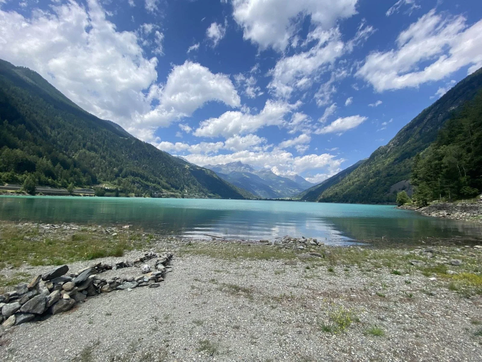 Lago di Poschiavo: Türkisblauer See umgeben von Bergen unter blauem Himmel mit Wolken.