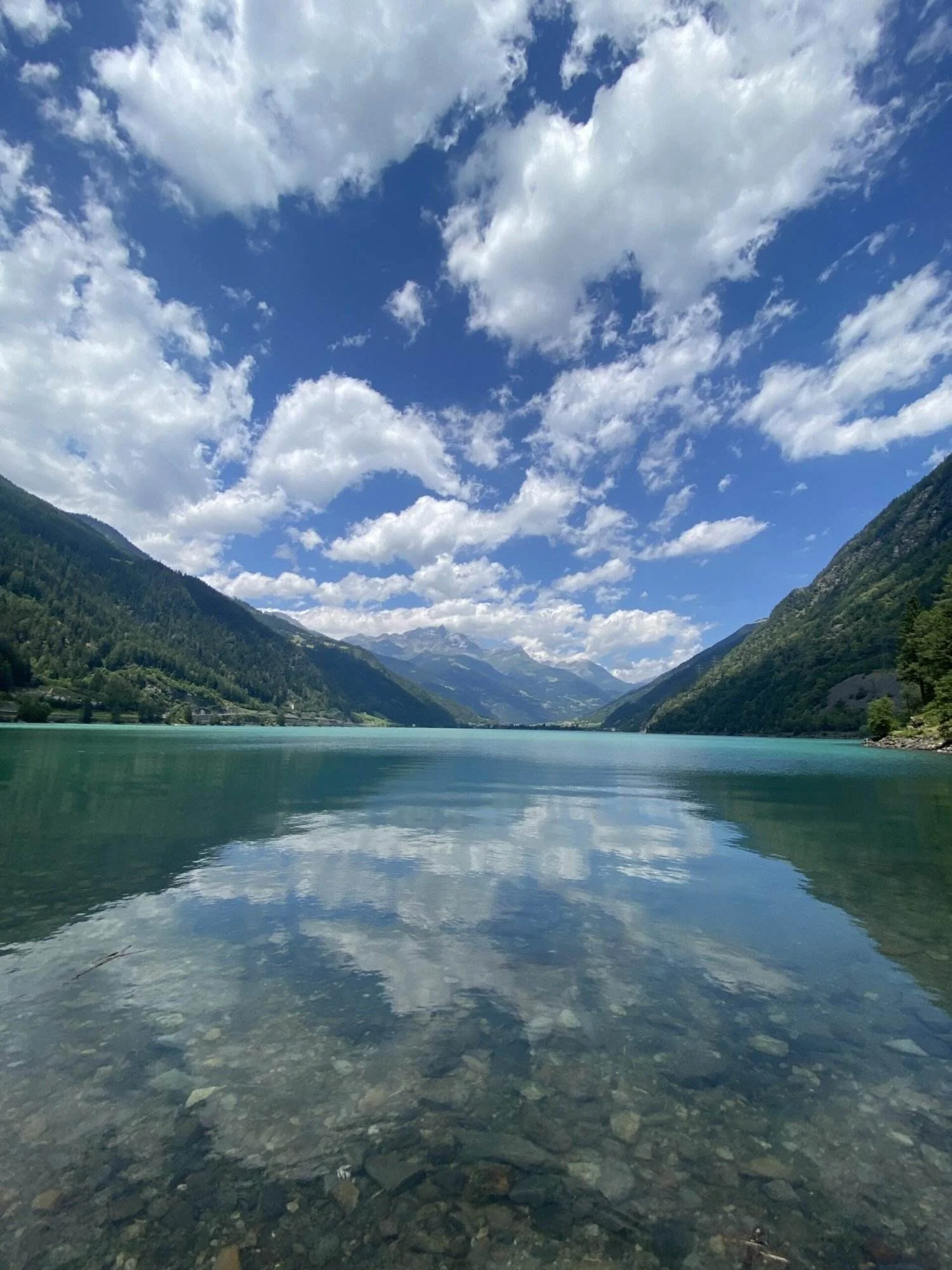 Lago di Poschiavo: Ruhiger Bergsee mit Spiegelung des Himmels und der Wolken.
